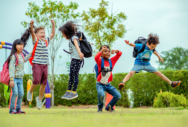 Five children on playground jumping up and down