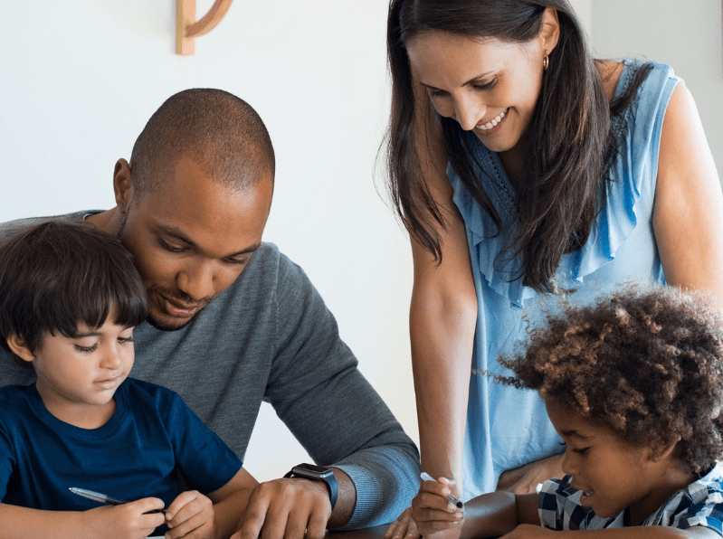 Two adults working with two children writing at a table